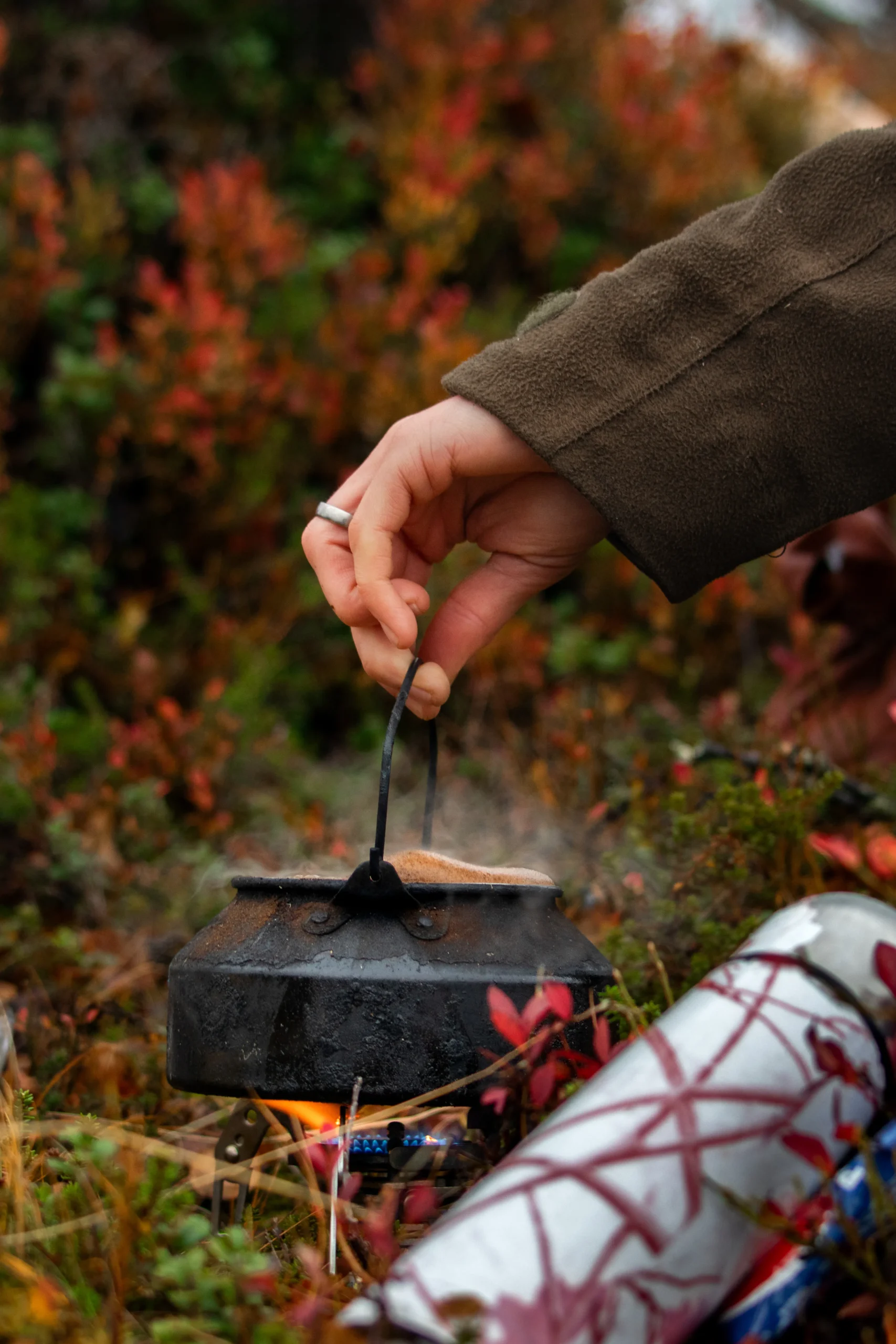 Man maakt koffie in de natuur met een ketel boven het vuur